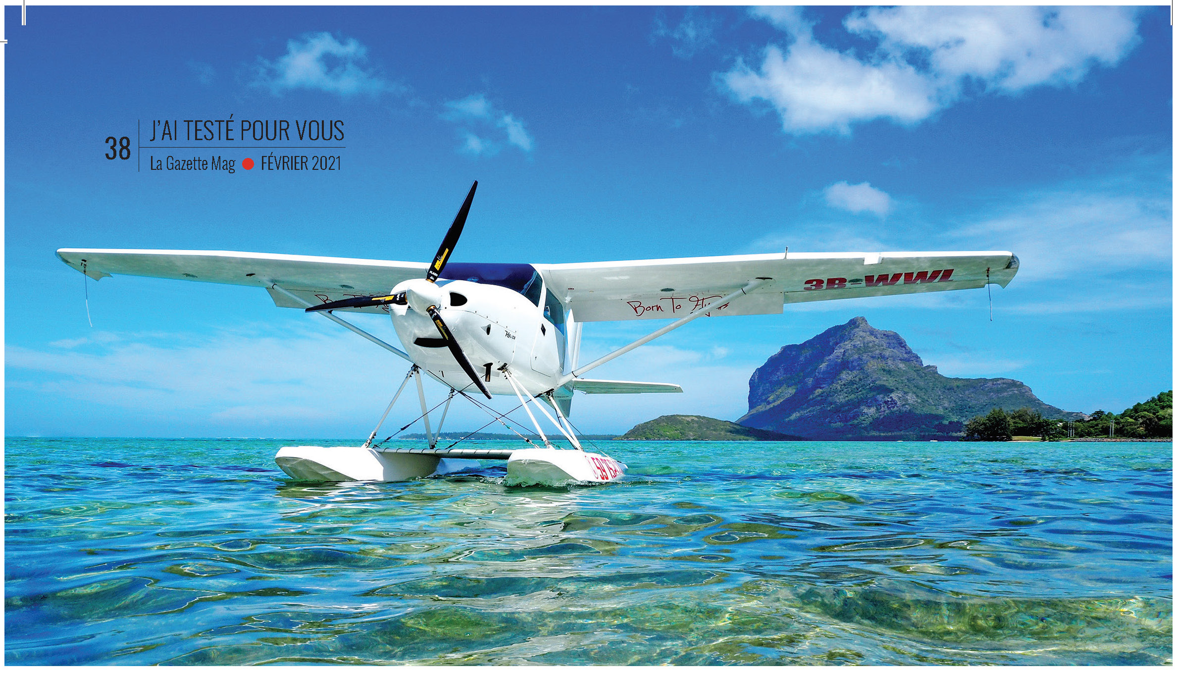 Hydravion sur les eaux claires d'une île tropicale, montagnes en arrière-plan, ciel dégagé, pour le magazine de février 2021.