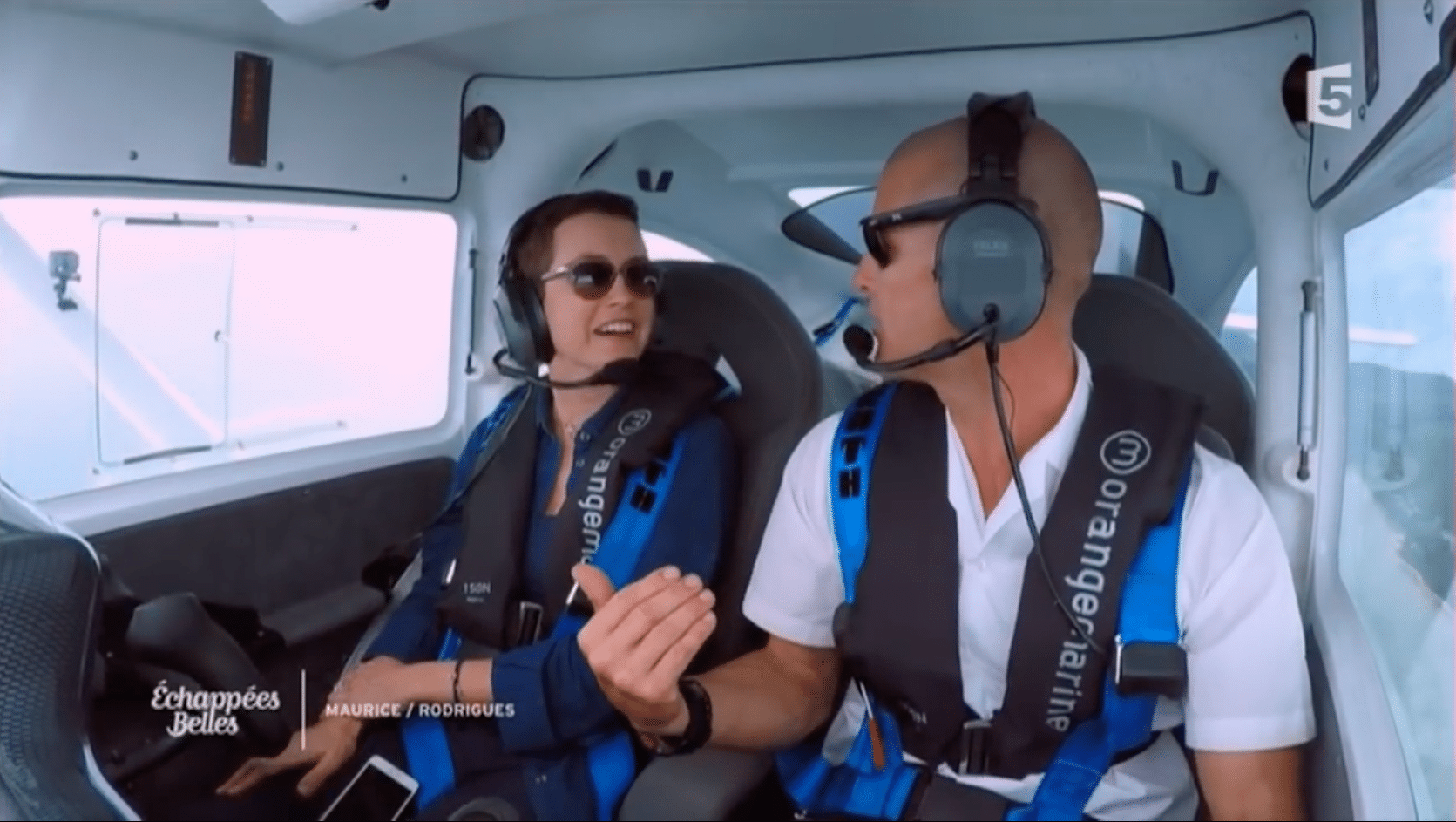 Two people in aircraft cockpit wearing headsets, discussing. "Échappées Belles" and "MAURICE/RODRIGUES".